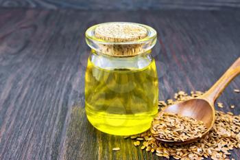 Linseed oil in a glass jar, flax seeds in a spoon against a dark wooden board