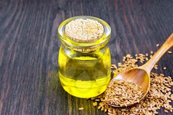 Linseed oil in a glass jar, flax seeds in a spoon on a wooden board background