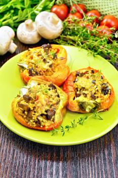 Pepper sweet, stuffed with mushrooms, tomatoes, couscous and cheese in a green plate on kitchen towel, fork, parsley against the background of dark wooden board