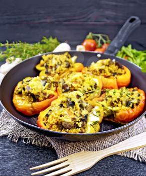 Pepper sweet, stuffed with mushrooms, tomatoes, couscous and cheese in an old frying pan on burlap, a fork, garlic, parsley and thyme against the background of black wooden board