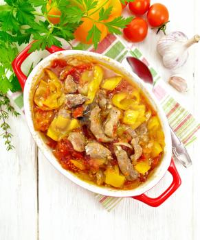 Ragout of turkey meat, tomato, yellow sweet pepper and onion with sauce in a brazier on a towel against a light wooden board on top