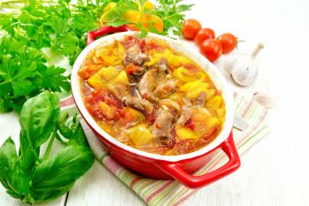 Ragout of turkey meat, tomato, yellow sweet pepper and onion with sauce in a red brazier on a napkin on a light wooden board background