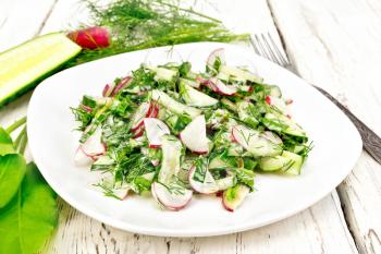 Salad of radish, cucumber, sorrel and greens, dressed with mayonnaise in a plate on the background of wooden board