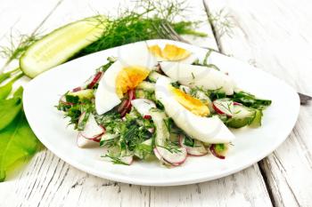 Salad from radishes, cucumber, sorrel, greens and eggs, dressed with mayonnaise and sour cream in a plate on the background of light wooden boards
