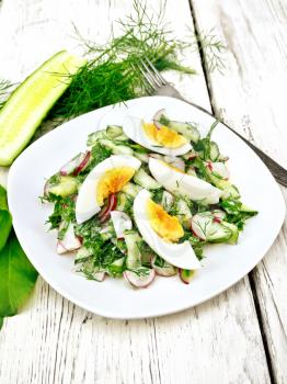 Salad from radish, cucumber, sorrel, greens and eggs, dressed with mayonnaise and sour cream in a plate on the background of light wooden table