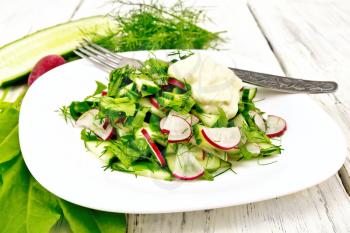 Salad of radish, cucumber, sorrel and greens, dressed with mayonnaise in a white plate on the background of wooden board