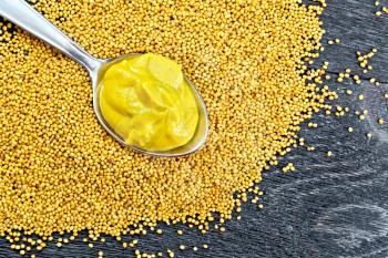 Mustard sauce in a metal spoon on mustard seeds against the background of a wooden board from above
