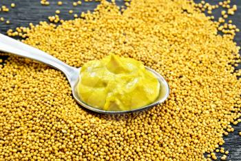 Mustard sauce in a metal spoon on mustard seeds against a black wooden board