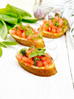 Bruschetta with tomato, basil and spinach, fresh spinach leaves, towel, garlic and vegetable oil in a carafe on the background of light wooden board