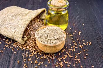Flax flour in a bowl, seeds in a bag and linen oil in a glass jar on a background of a dark wooden board