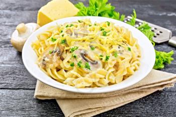 Fusilli pasta with mushrooms in creamy sauce, parsley and grated cheese in a plate on napkin on wooden board background