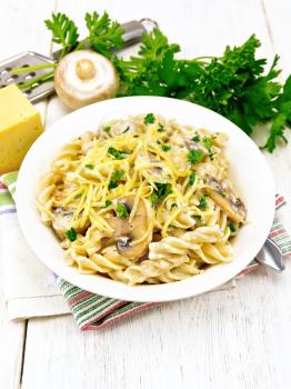 Fusilli pasta with champignons in creamy sauce, parsley and grated cheese in a dish on kitchen towel against light wooden board