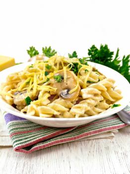 Fusilli pasta with mushrooms in creamy sauce, parsley and grated cheese in a dish on kitchen towel against light wooden board