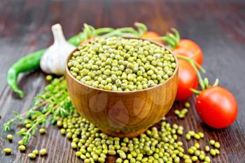 Green lentils mung in a bowl, hot peppers, garlic, thyme and red tomatoes on a wooden board background
