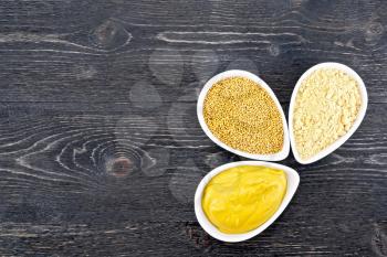 Mustard sauce, seeds and mustard powder in three saucepans on a wooden plank background
