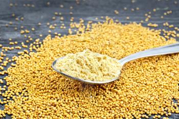 Mustard powder in a metal spoon on the seeds against the background of a wooden board
