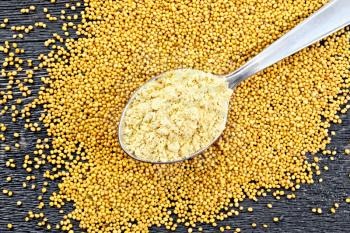 Mustard powder in a metal spoon on the seeds against a wooden plank top