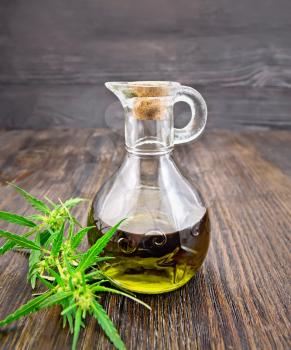 Hemp oil in a glass decanter, cannabis leaves on a wooden board background