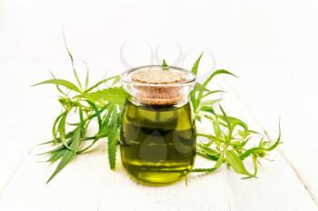 Hemp oil in a glass jar, leaves and stalks of cannabis on the background of light wooden boards