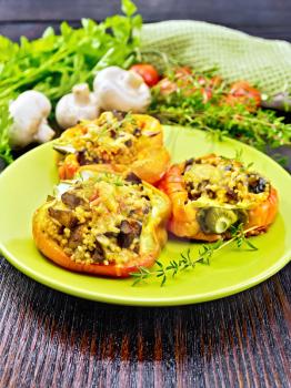 Pepper sweet, stuffed with mushrooms, tomatoes, couscous and cheese in a green plate on kitchen towel, a fork, parsley against the background of wooden board