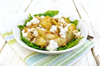 Salad of fried pear, spinach, salted feta cheese and cedar nuts in a plate on a towel against the backdrop of a wooden board
