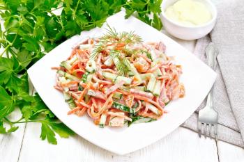Salad from smoked sausage, spicy carrot, tomato, cucumber and spices, dressed with mayonnaise, kitchen towel, fork and parsley on a wooden board background