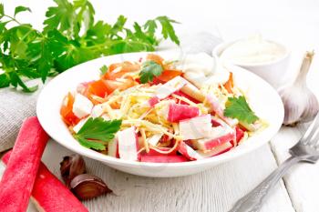 Salad of crab sticks, cheese, garlic, tomatoes and mayonnaise, kitchen towel, parsley on the background of a light wooden board