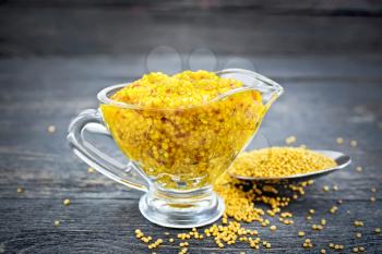 Mustard Dijon sauce in a glass sauceboat and mustard seeds in a spoon on a black wooden board background