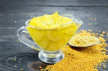 Mustard sauce in a glass sauceboat, seeds and mustard powder in a spoon on a wooden board background