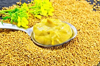Mustard sauce in a metal spoon with a yellow flower on mustard seeds against the background of a wooden board