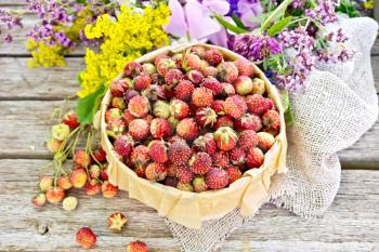 Wild ripe strawberries in a bark box with parchment, burlap and wild flowers on the background of old wooden boards