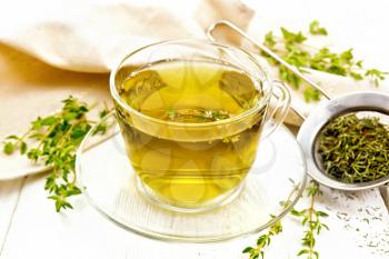 Herbal tea in a glass cup of thyme, a metal strainer with dry leaves, a linen napkin on the background of a light wooden board