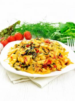 Cabbage stew with leaf beets and tomatoes in a white plate on a napkin, parsley and fork on light wooden board background