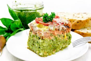 Casserole of salmon and rice with pesto, tomato and cheese in plate, bread, garlic and a jar of sauce on wooden board background