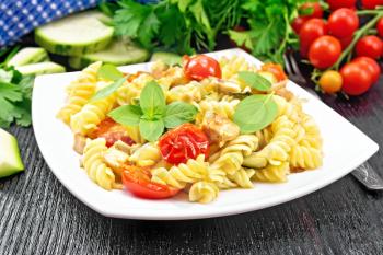Fusilli with chicken, zucchini and tomatoes in a plate, napkin, fork, basil and parsley on wooden board background