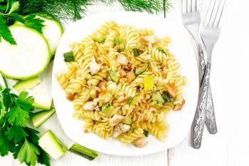 Fusilli pasta with chicken breast, zucchini, cream and pine nuts in a plate, fork and parsley on a wooden board background from above