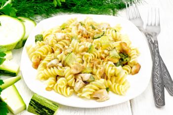 Fusilli pasta with chicken breast, zucchini, cream and pine nuts in a plate, fork and parsley on the background of a light wooden board

