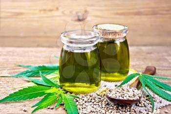 Hemp oil in two glass jars with grain in a spoon and on the table, cannabis leaves on the background of an old wooden board
