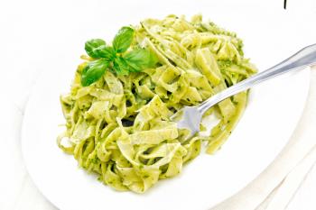 Tagliatelle pasta with pesto, basil and fork in a plate on a napkin on white wooden board background