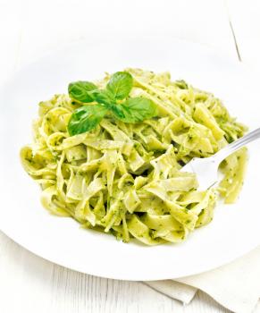 Tagliatelle pasta with pesto, basil and fork in a plate on a napkin on wooden board background