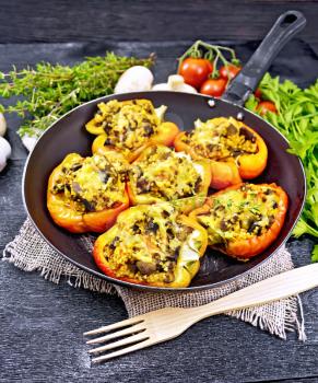 Pepper sweet, stuffed with mushrooms, tomatoes, couscous and cheese in an old frying pan on burlap, a fork, parsley and thyme against the background of wooden board