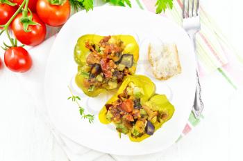 Sweet pepper stuffed with mushrooms, tomatoes, zucchini, eggplant and onions, seasoned with wine, garlic, thyme and spices in white plate on kitchen towel on background of wooden board from above