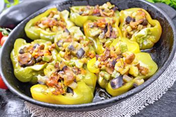 Sweet pepper stuffed with mushrooms, tomatoes, zucchini, eggplant and onions, seasoned with wine, garlic, thyme and spices in a frying pan on a napkin of burlap on wooden board background