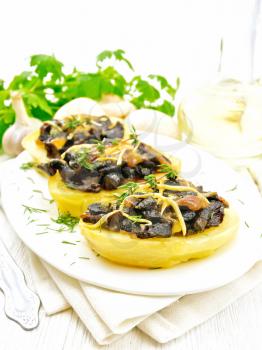 Potatoes stuffed with mushrooms, fried onions and cheese in a plate on napkin, vegetable oil in carafe, parsley, garlic and a fork on background of white wooden board