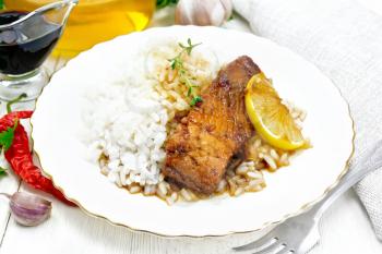 Pink salmon with honey, lemon juice and soy sauce, boiled rice, slice of lemon and a sprig of thyme in a plate, hot pepper, garlic, parsley, napkin and fork on wooden board background