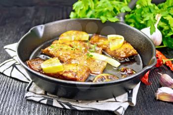 Pink salmon with a sauce of honey, lemon juice, garlic, hot pepper and soy sauce, lemon slices and a sprig of thyme in a frying pan on a napkin, parsley on wooden board background