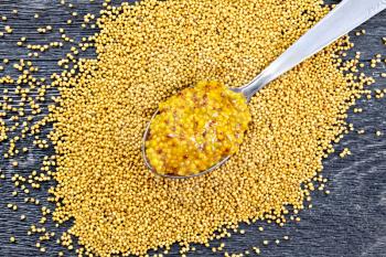Mustard Dijon sauce in a metal spoon on the seeds on a wooden board background on above