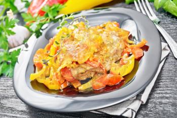 Chicken stewed with tomatoes, yellow and red bell peppers and cheese in a plate on kitchen towel, thyme, thyme, parsley and garlic on wooden board background