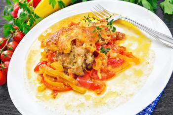 Chicken stewed with tomatoes, yellow and red bell peppers and cheese in white plate on a napkin, thyme, parsley and garlic on black wooden board background