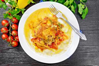 Chicken stewed with tomatoes, yellow and red bell peppers and cheese in white plate on a napkin, thyme, parsley and garlic on wooden board background from above